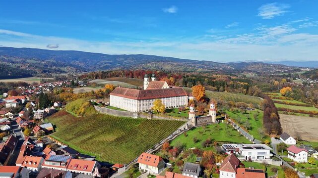 Aerial view of Schloss Stainz surrounded by vineyards and autumn foliage in the rolling hills of the Weststeiermark region in Stainz, Styria, Austria.