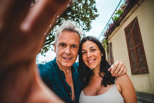 Affectionate couple takes a spontaneous selfie while exploring a charming old town on vacation. Direct eye contact and a warm embrace capture authentic love and shared travel memories.