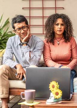 Disappointed gen z friends watch troubling content on a laptop while sitting together indoors on a couch during a quiet break. Their expressions convey bad news, digital fatigue, and discomfort.