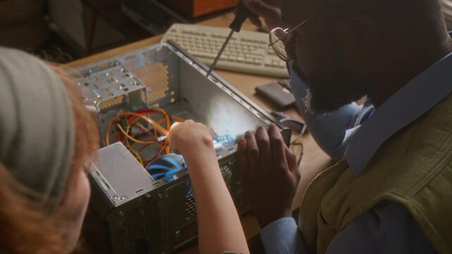 Over the shoulder shot of African American man and Caucasian woman repairing desktop computer tower, unscrewing graphics card. Clip is perfect for IT support services and tech education promos