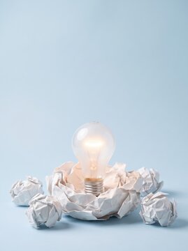 Glowing lightbulb in crumpled paper nest on blue background