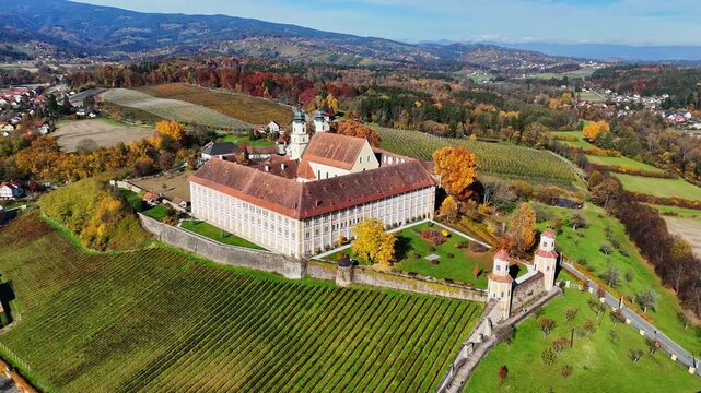 Aerial view of the historic Schloss Stainz monastery surrounded by lush autumn vineyards and rolling hills in Stainz, Styria, Austria.