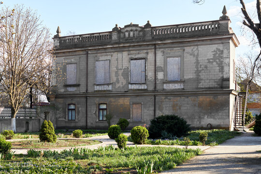 Abandoned historic building with boarded windows and overgrown garden in daylight