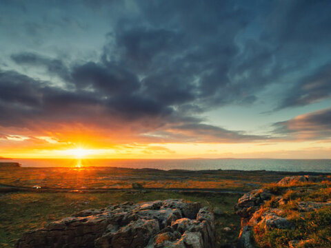 Sunset scene, view from a rough stone hill on a field and sunset sky over ocean. Famous Burren area of Ireland. Hot and warm sun glow. Calm and relaxing view.