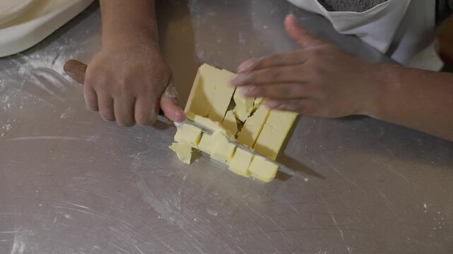 Indigenous child cutting butter with a knife on a metal table for making bread; malnutrition syndrome