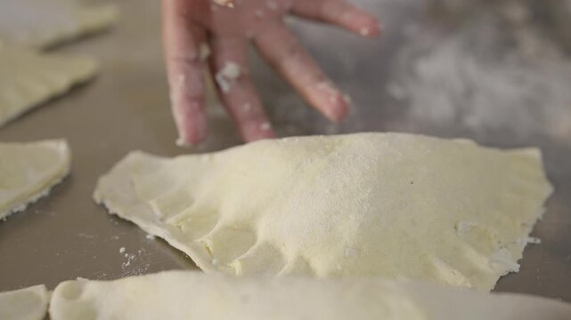 Detail of a girl's hands kneading and preparing a cheese-filled empanada on a kitchen table