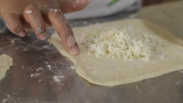 Detail of a girl's hands kneading and preparing a cheese-filled empanada on a kitchen table
