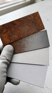 Hand in glove holding metal plates showing sandblasting process stages. Comparison of rusty steel surface cleaning. Industrial maintenance, metal restoration and surface preparation test.