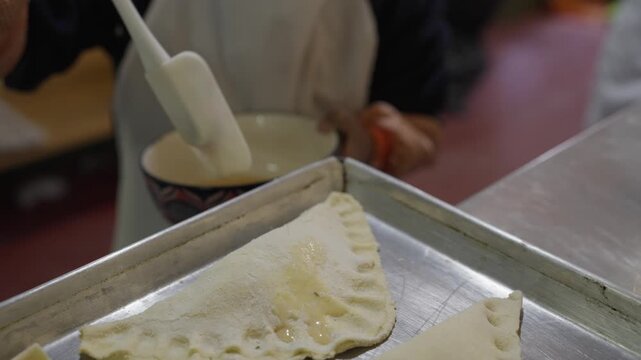 Detail of a girl's hands kneading and preparing a cheese-filled empanada on a kitchen table