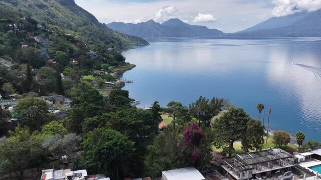 Aerial view of Lake Atitlan with the town of Santiago Atitlan, lush green hills, and a swimming pool along the shoreline in Santiago Atitlan, Solola Department, Guatemala.