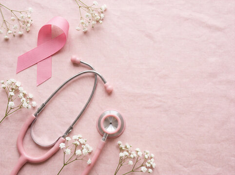 Pink ribbon and stethoscope with delicate white flowers on soft fabric for Breast Cancer Awareness Month copy space