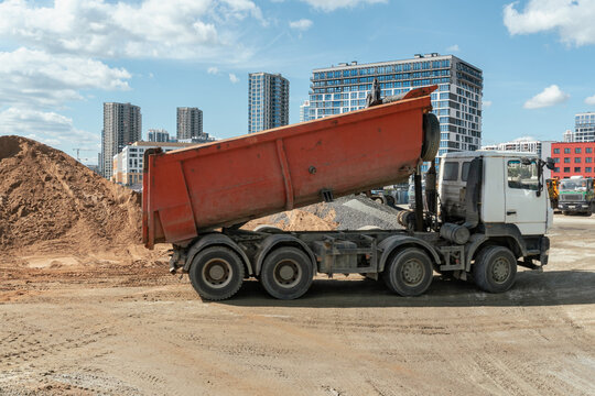 Heavy tipper truck with raised orange dumper body operating at modern city construction site. This commercial image is ideal for real estate development, logistics and industrial machinery