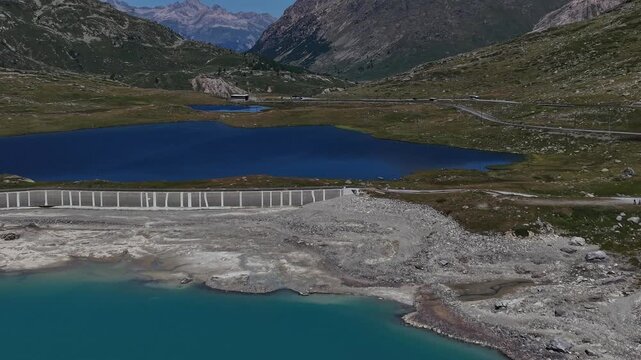 Aerial view of the turquoise Lago Bianco reservoir and its dams nestled among the rugged alpine mountains of the Bernina Pass in Poschiavo, Grisons, Switzerland.