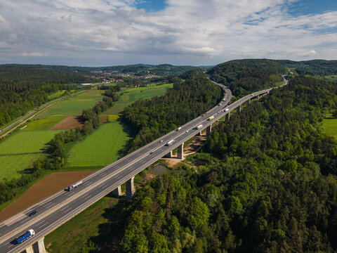 Aerial view of the A9 motorway viaduct near Hedersdorf, with traffic flowing across the concrete bridge surrounded by lush forests and fields in Schnaittach, Bayern, Germany.