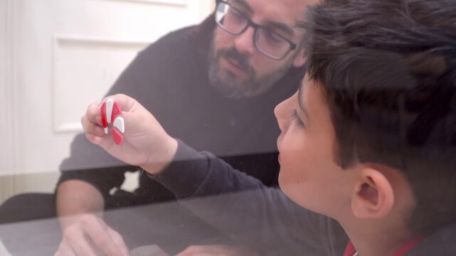 father and son assembling sugar cane decoration on home glass door for christmas