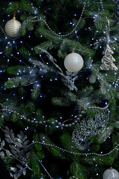 Green Christmas tree with white and silver baubles and glittery leaves Silver bead garlands wrap branches with LED lights glowing in dark background creating festive holiday mood