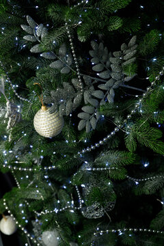 Closeup of green Christmas tree with white pearl bauble and silver glittery leaves Small LED lights glow among needles creating festive holiday atmosphere with dark background