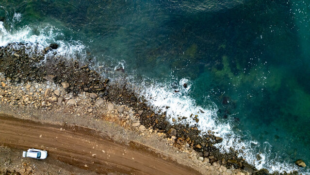 A car on a gravel road seen from a drone as size comparison for the sea in the fjord in Iceland