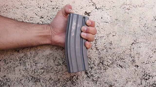 Close up video of a person unloading rifle cartridges from a detachable rifle magazine by pressing each round forward with a finger, demonstrating safe ammunition handling outdoors.