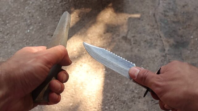 Close up video of a person sharpening a hunting knife with a sharpening steel outdoors, demonstrating proper blade maintenance and edge honing with precise hand movements.