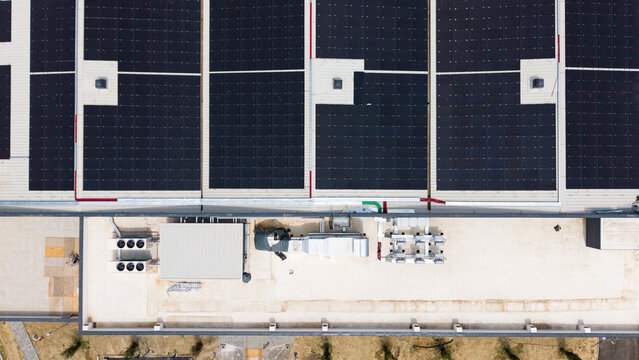Aerial view of a modern logistics hub featuring extensive rooftop solar panel arrays, industrial ventilation systems and HVAC units on a flat roof in Melegnano, Lombardy, Italy.