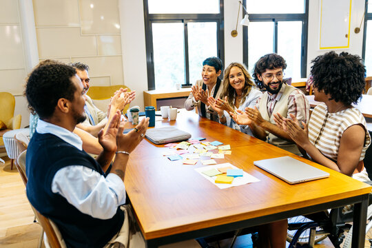 Diverse group of professionals clapping hands at a meeting table, celebrating achievements and collaboration in a modern office