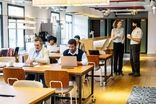 Diverse professionals networking and working in a modern open plan shared office, using technology and discussing ideas