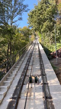 Funicular railway track ascending steep hill surrounded by green trees under clear blue sky