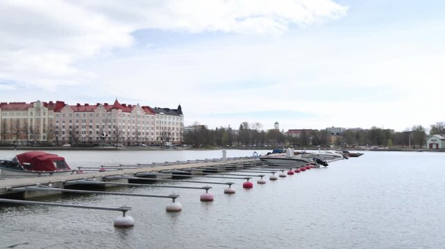 Close up of a barnacle goose taking off and flying above a calm lake with elegant buildings and a marina filled with boats in the background capturing dynamic urban wildlife