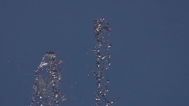 Super slow motion of water droplets splashing from a fountain against a clear blue sky