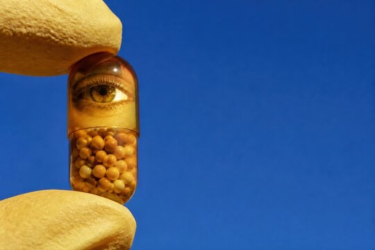 Surreal capsule with eye and beads held by gloved hands on blue background