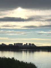 Fototapeta premium Dramatic cloudy sky over modern city skyline reflecting in river water surface on peaceful overcast day