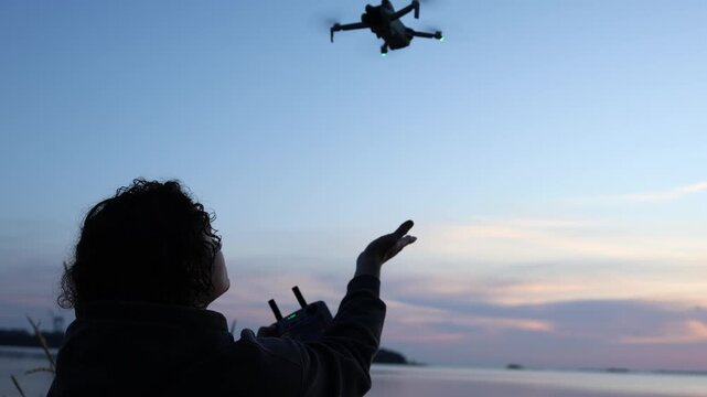 Drone hovering in the air as a young man reaches out his hand for the drone to land capturing a smooth aerial technology interaction outdoors