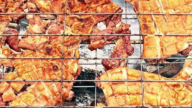 Traditional roasted pork belly with crispy skin cooking on a metal grill over charcoal.