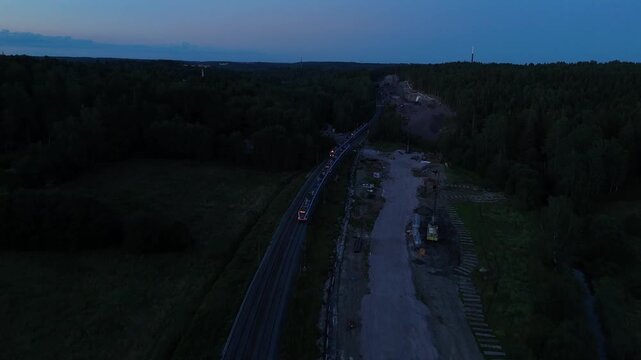 Aerial drone view of two trains passing each other on parallel railway tracks in the evening surrounded by a peaceful forest landscape and fading daylight
