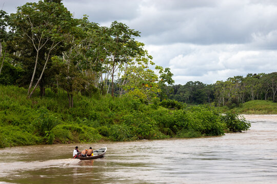 Small wooden boat navigating a muddy river past dense green rainforest trees at Parque Ecologico Januari in Manaus