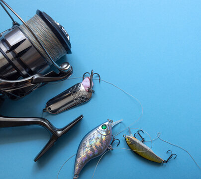 Close‑up of a metallic fishing reel and three detailed lures on a light blue background. The composition highlights craftsmanship, technique, and the beauty of modern fishing gear.