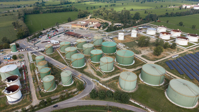 Aerial view of the Sigemi S.r.l. industrial facility featuring numerous large green storage tanks, white tanks, and solar panels surrounded by lush green fields in Lacchiarella, Lombardia, Italy.