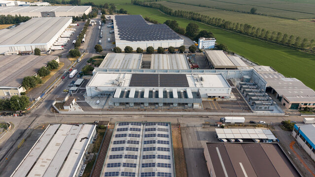 Aerial view of the Stack Infrastructure MIL03 data center, featuring industrial warehouses with solar panels on rooftops, surrounded by roads and fields in Siziano, Lombardia, Italy.