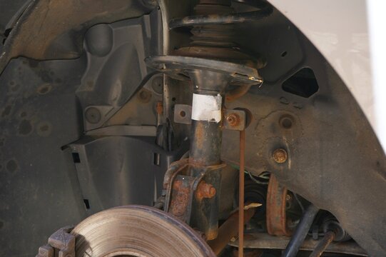 Close-up of a worn suspension strut with rusty coil spring inside a vehicle wheel arch. Concept of automotive repair, suspension inspection, shock absorber replacement and car maintenance.