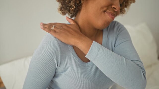 Woman rubbing shoulder on studio bed, hand showing rings and gentle smile; relief self care recovery.