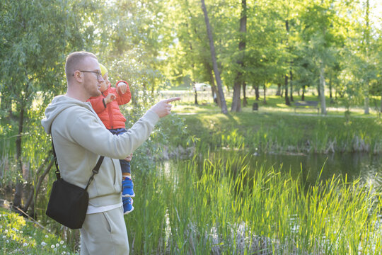 Father with his little son staying near lake and father pointing with his finger at something.