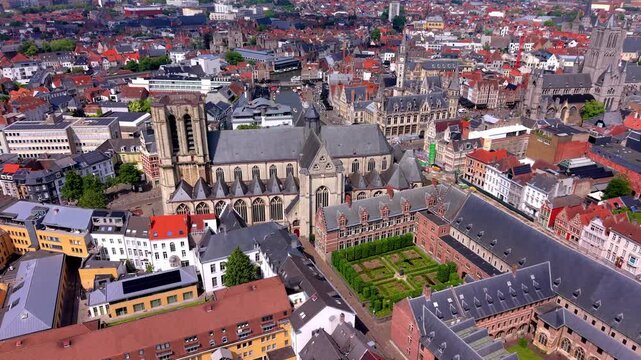 Aerial view video clip of Saint Michael's Church in Ghent, Belgium, featuring inner courtyard garden, Graslei canal, and red roofed medieval cityscape on a sunny day