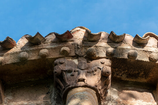 Detail of a 12th century Romanesque carved stone capital displaying a human figure and masks on a column under the eaves of San Martin de Tours church, located in Vizcainos, Burgos, Spain