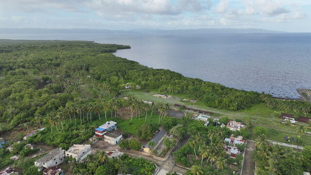 Aerial view of the coastal town featuring lush palm trees, dense tropical vegetation, and small residential houses along the shoreline in Sabana de la Mar, Hato Mayor Province, Dominican Republic.