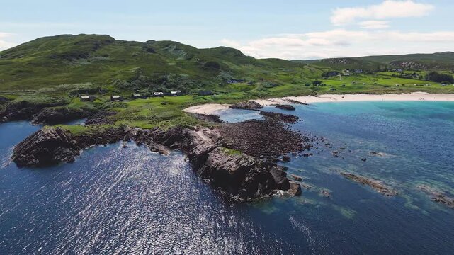 Aerial flight around rocky headlands and clear tidal water at Mellon Udrigle Beach, opening onto the broad sandy bay and green hills of Wester Ross