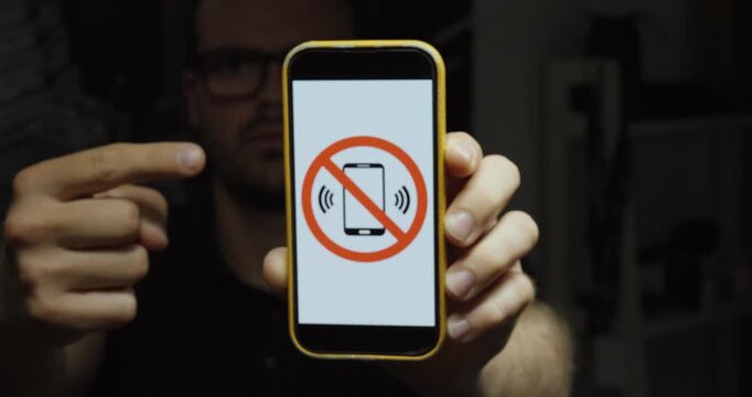 Person pointing at a smartphone displaying a no mobile phone symbol. Ideal for phone restrictions, mobile-free zones, digital detox, and policy concepts.