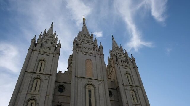 Facade of the Mormon Temple in Salt Lake City, Utah with wispy clouds gently passing over the spires of the temple on Temple Square.  Gothic style architecture completed in 1893.  