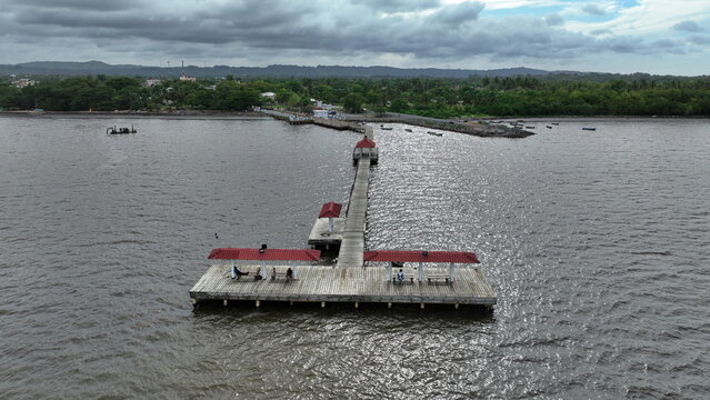 Aerial view of the wooden pier with red-roofed shelters, calm waters, and lush green coastline in Sabana de la Mar, Hato Mayor Province, Dominican Republic.