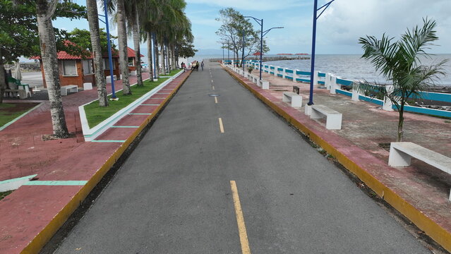 Aerial view of the coastal boardwalk lined with palm trees and benches leading toward the sea in Sabana de la Mar, Hato Mayor Province, Dominican Republic.